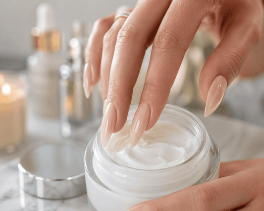 Fingers with long fingernails painted in soft pink dipping into a jar skincare.