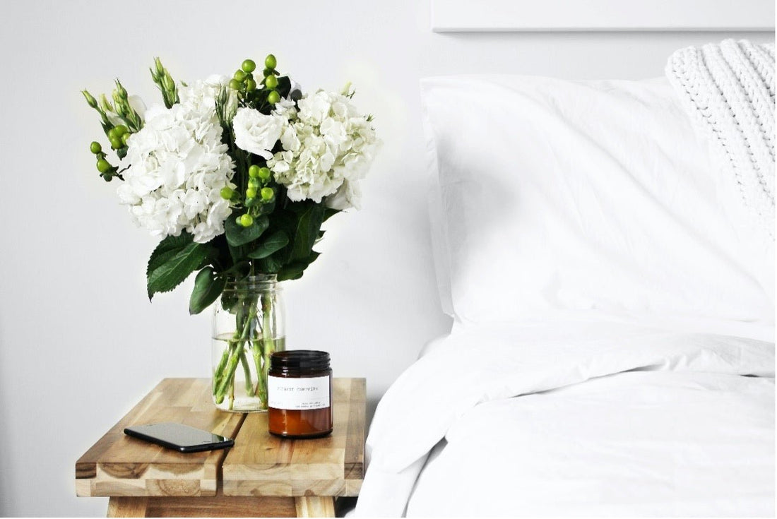 Picture of a bed with a vase of flowers, a candle, and a phone on the bedside table.